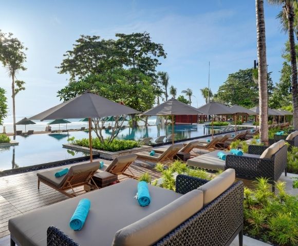 Resort poolside with lounge chairs, umbrellas, and a pool overlooking a beach.
