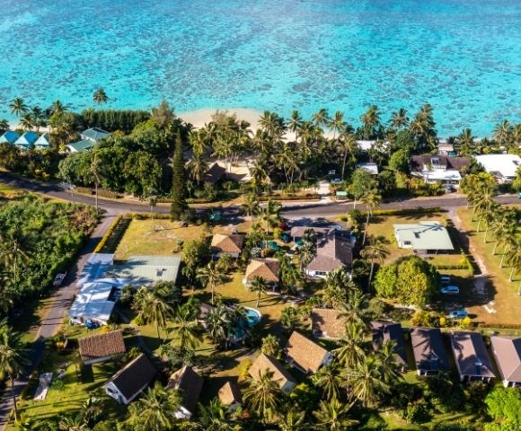 Aerial view of tropical beachfront property surrounded by trees and nearby buildings
