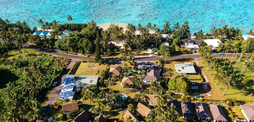 Aerial view of tropical beachfront property surrounded by trees and nearby buildings