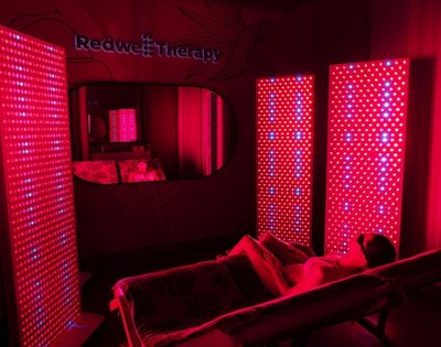 Person relaxing on a lounge chair surrounded by red LED light panels in a dimly lit red therapy room.