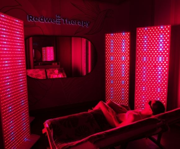 Person relaxing on a lounge chair surrounded by red LED light panels in a dimly lit red therapy room.