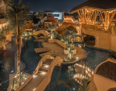Aerial nighttime view of a resort pool surrounded by warm lighting, pathways, and tropical architecture