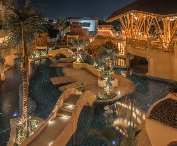 Aerial nighttime view of a resort pool surrounded by warm lighting, pathways, and tropical architecture