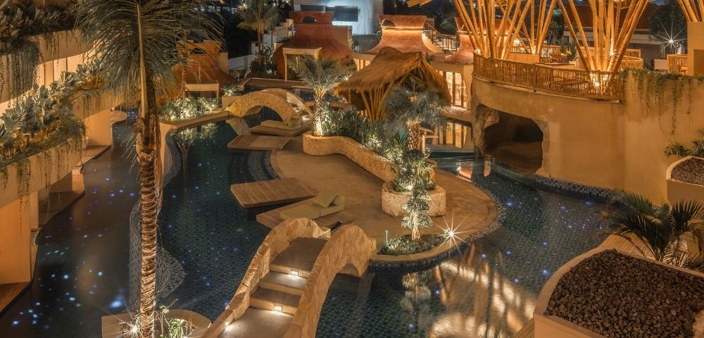 Aerial nighttime view of a resort pool surrounded by warm lighting, pathways, and tropical architecture