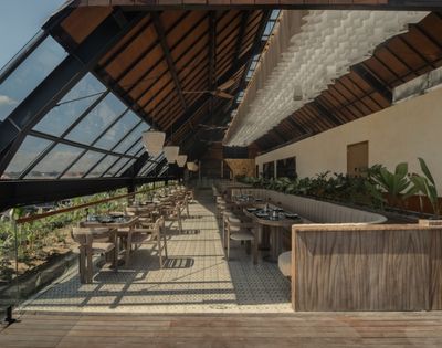 Covered restaurant space with wooden furnishings, high ceilings, and views of tropical greenery