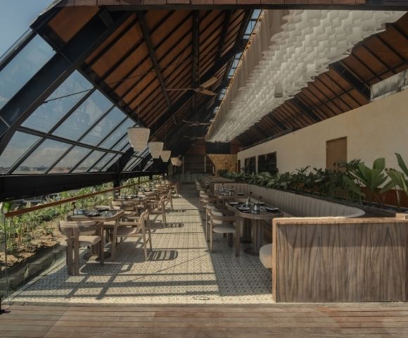 Covered restaurant space with wooden furnishings, high ceilings, and views of tropical greenery