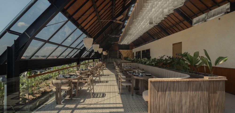 Covered restaurant space with wooden furnishings, high ceilings, and views of tropical greenery