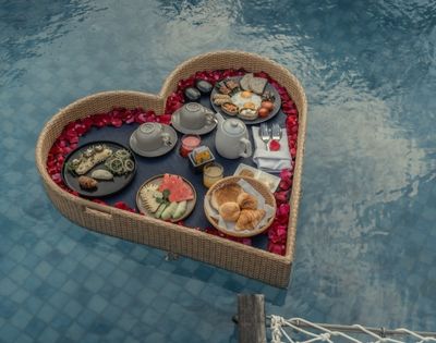 Heart-shaped floating breakfast tray with pastries, fruit, and beverages in a swimming pool