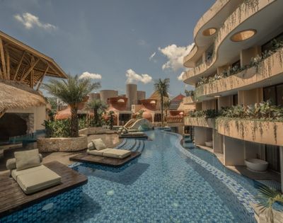 Resort swimming pool lined with sun loungers, palm trees, and modern buildings