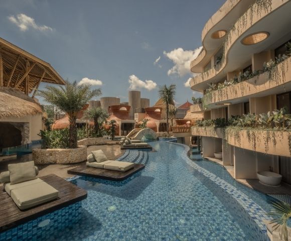 Resort swimming pool lined with sun loungers, palm trees, and modern buildings