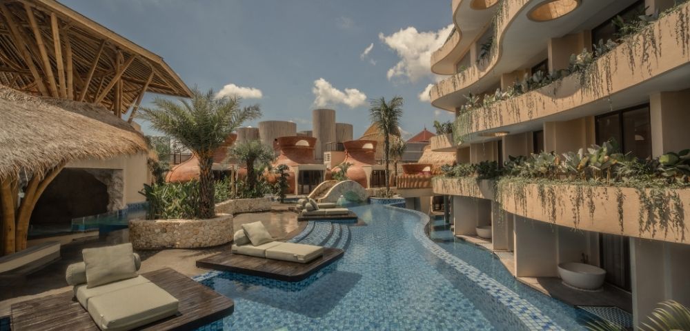 Resort swimming pool lined with sun loungers, palm trees, and modern buildings