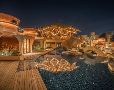 Resort pool illuminated at night with reflections of architectural lighting on the water