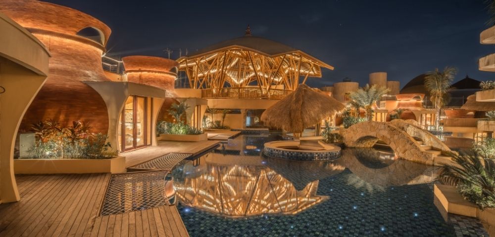 Resort pool illuminated at night with reflections of architectural lighting on the water