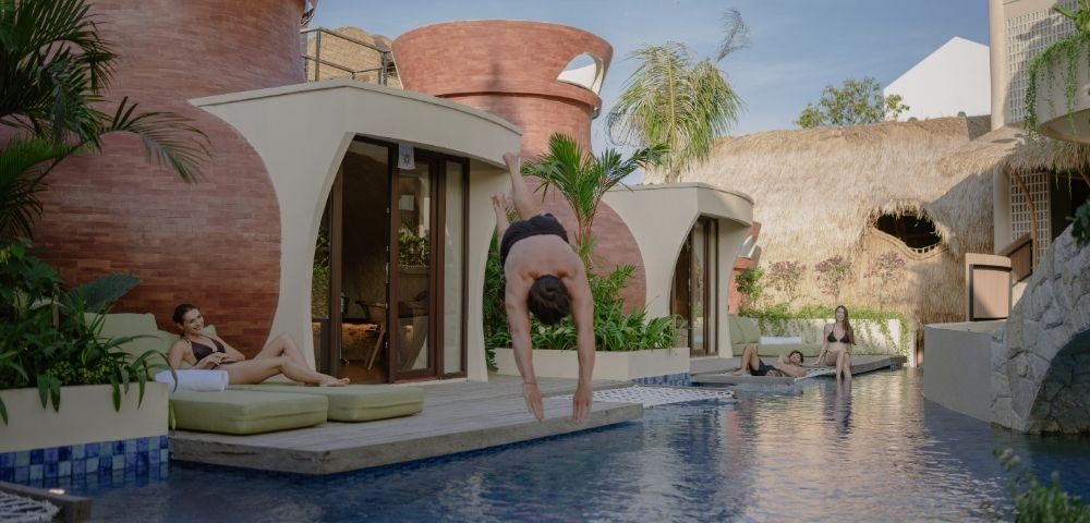 Resort swimming pool framed by contemporary architecture, tropical plants, and shaded seating