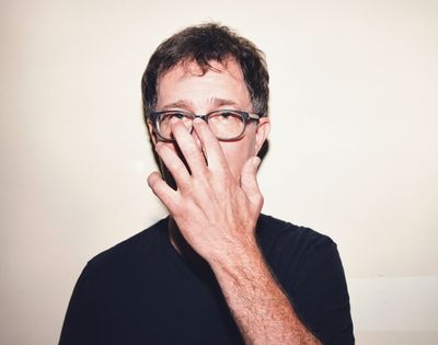 Man wearing glasses, with his hand covering the bridge of his nose.