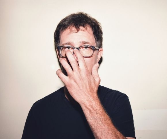 Man wearing glasses, with his hand covering the bridge of his nose.