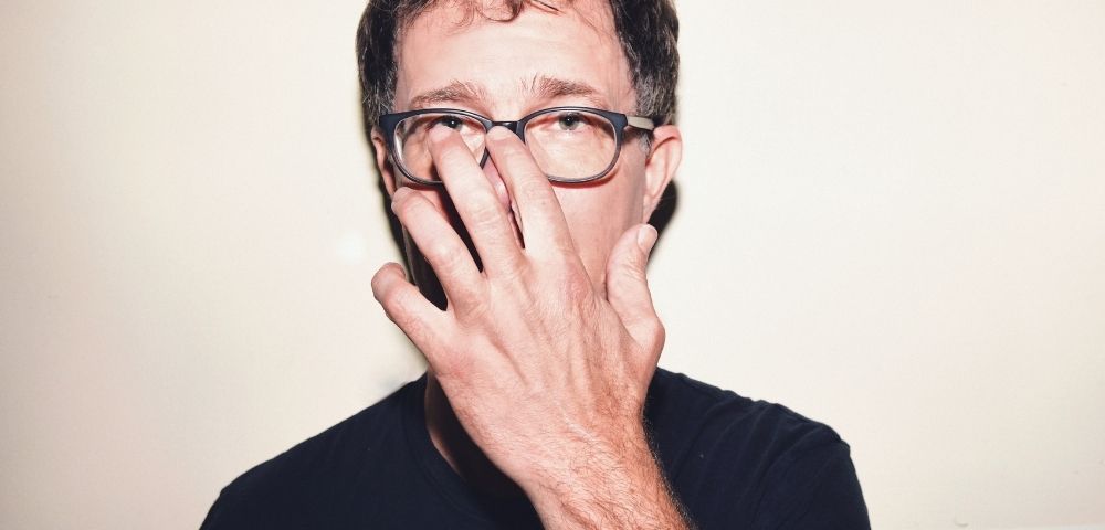 Man wearing glasses, with his hand covering the bridge of his nose.