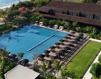 Aerial view of a large outdoor swimming pool with sun loungers and black umbrellas lined up on the deck beside a green lawn.