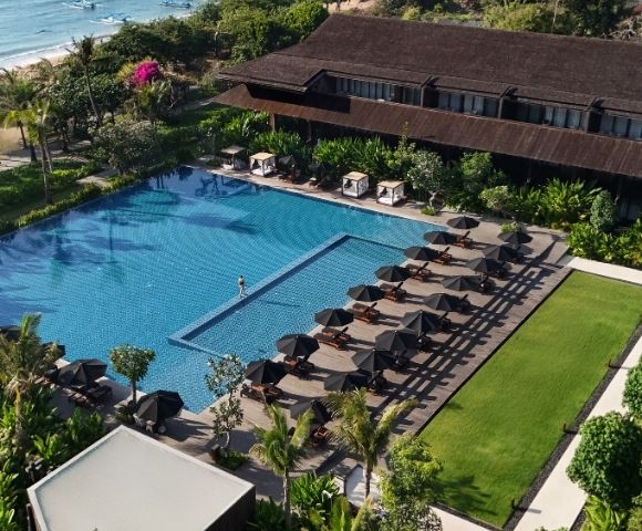 Aerial view of a large outdoor swimming pool with sun loungers and black umbrellas lined up on the deck beside a green lawn.
