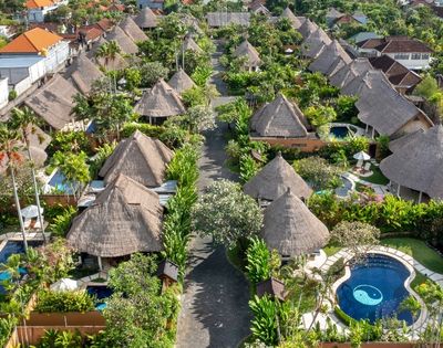 Aerial view of a resort complex with thatched-roof bungalows, swimming pools, and lush tropical landscaping.