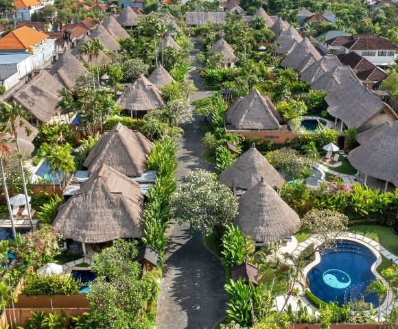 Aerial view of a resort complex with thatched-roof bungalows, swimming pools, and lush tropical landscaping.