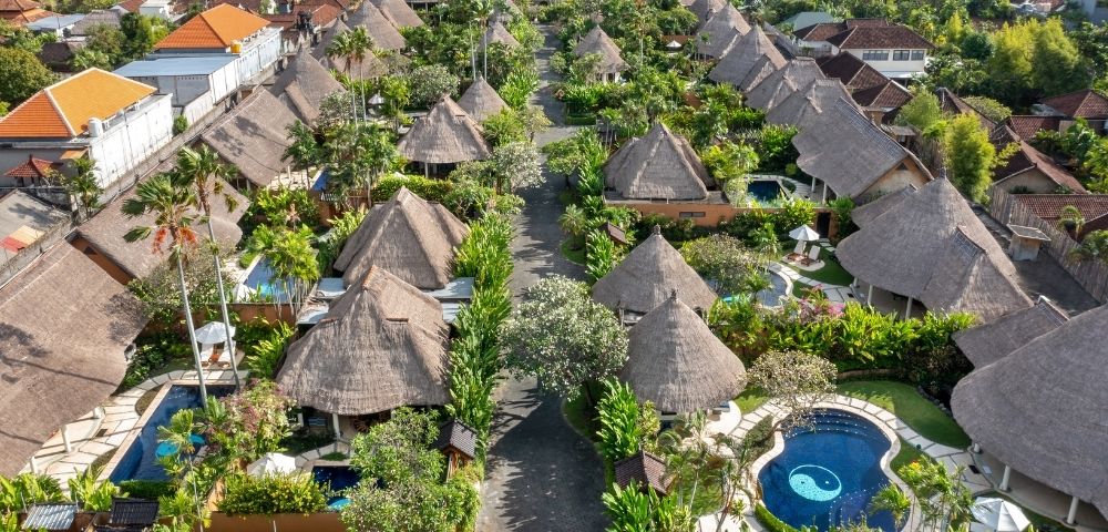 Aerial view of a resort complex with thatched-roof bungalows, swimming pools, and lush tropical landscaping.