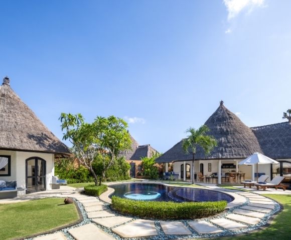 Resort bungalows with thatched roofs surrounding a swimming pool with a yin and yang design.