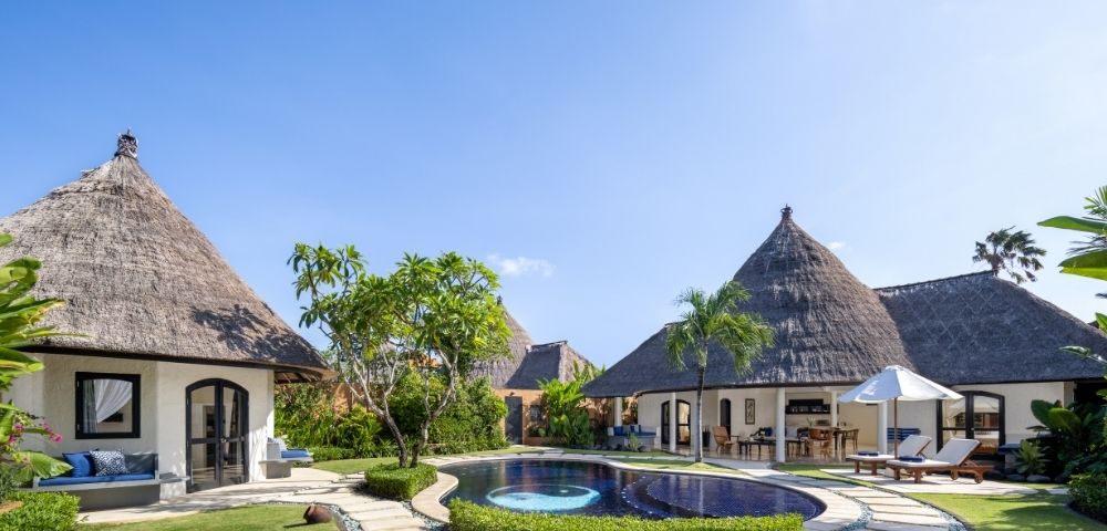 Resort bungalows with thatched roofs surrounding a swimming pool with a yin and yang design.
