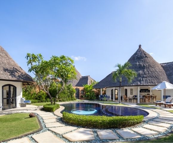 Resort bungalows with thatched roofs surrounding a swimming pool with a yin and yang design.