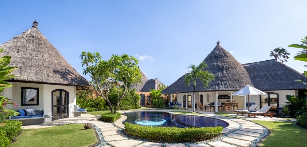 Resort bungalows with thatched roofs surrounding a swimming pool with a yin and yang design.