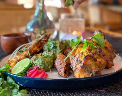 A platter of Indian kebabs and grilled chicken with lime wedges and cilantro.