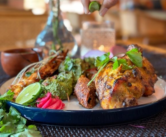 A platter of Indian kebabs and grilled chicken with lime wedges and cilantro.