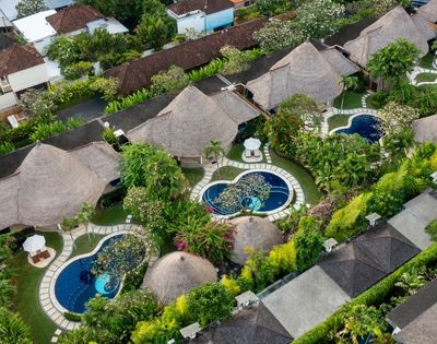 Aerial view of a tropical resort with thatched-roof bungalows, private swimming pools, and lush greenery.