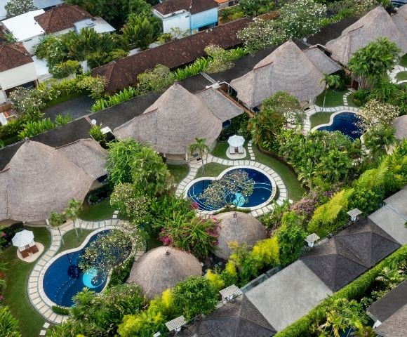 Aerial view of a tropical resort with thatched-roof bungalows, private swimming pools, and lush greenery.