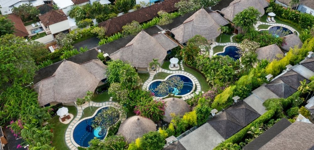 Aerial view of a tropical resort with thatched-roof bungalows, private swimming pools, and lush greenery.