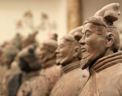 Close-up profile of a terracotta warrior statue, with more statues blurred in the background, showcasing ancient Chinese artistry.