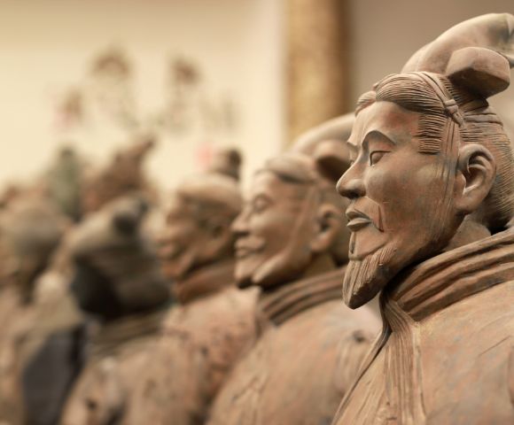 Close-up profile of a terracotta warrior statue, with more statues blurred in the background, showcasing ancient Chinese artistry.