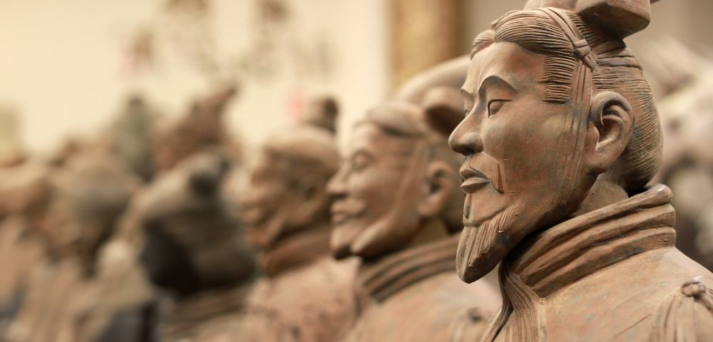 Close-up profile of a terracotta warrior statue, with more statues blurred in the background, showcasing ancient Chinese artistry.