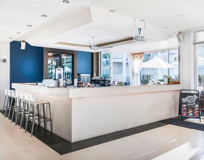 A bright, modern bar with a white counter, bar stools, and a dark blue accent wall, featuring a 