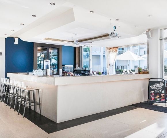 A bright, modern bar with a white counter, bar stools, and a dark blue accent wall, featuring a 