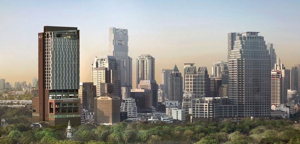 City skyline with modern skyscrapers behind a large green park under a clear sky at sunset.
