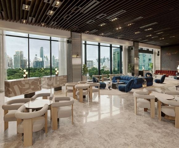 Spacious modern lounge with floor-to-ceiling windows, beige chairs, blue sofas, marble floors, and city skyline views in the background.