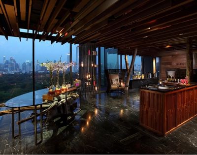 A modern interior of a spa or wellness center featuring sleek wooden decor, large windows showcasing a city view, and a reception area with candles and plants.