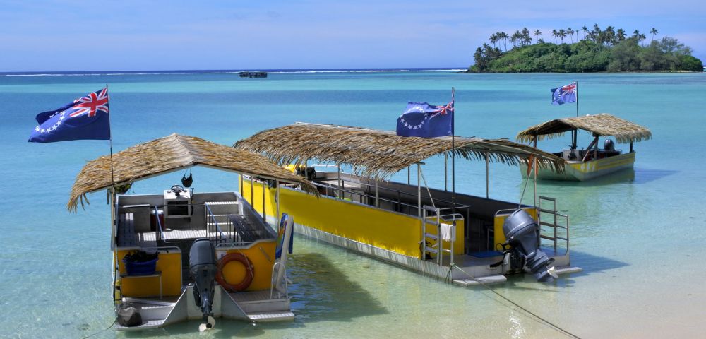 Two flat-bottomed boats with thatched roofs and outboard motors sit in crystal-clear turquoise water near a sandy beach.