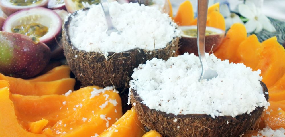 Two halves of a coconut shell filled with shredded coconut, surrounded by sliced mango and passion fruit.