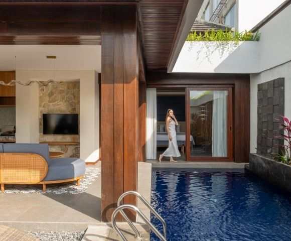 A woman in a white dress walks out of a room with a bed towards a private swimming pool.
