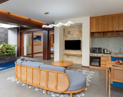 A modern living space with a curved gray sofa, a small plunge pool with a waterfall, a kitchenette, and a dining area.