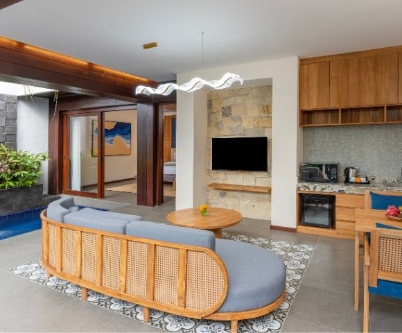 A modern living space with a curved gray sofa, a small plunge pool with a waterfall, a kitchenette, and a dining area.