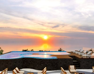 Infinity pool overlooking the ocean at sunset, with lounge seating and colorful evening skies.