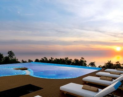 Rooftop infinity pool with sun loungers and ocean views during sunset, creating a relaxing resort atmosphere.